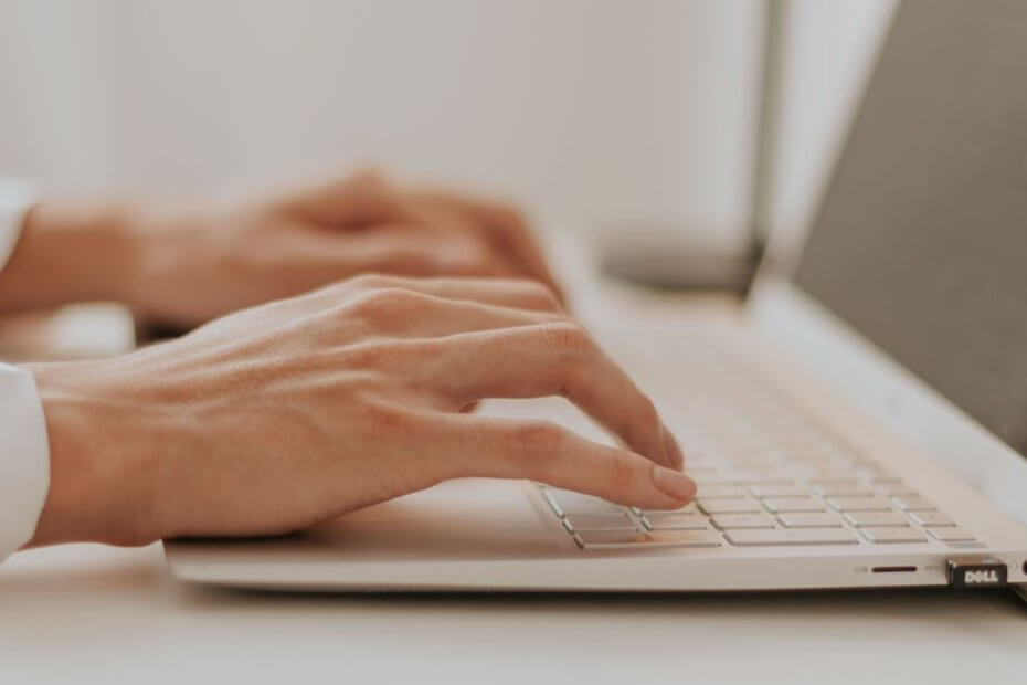 Close-up of hands typing on a laptop in a bright minimalistic office setting.